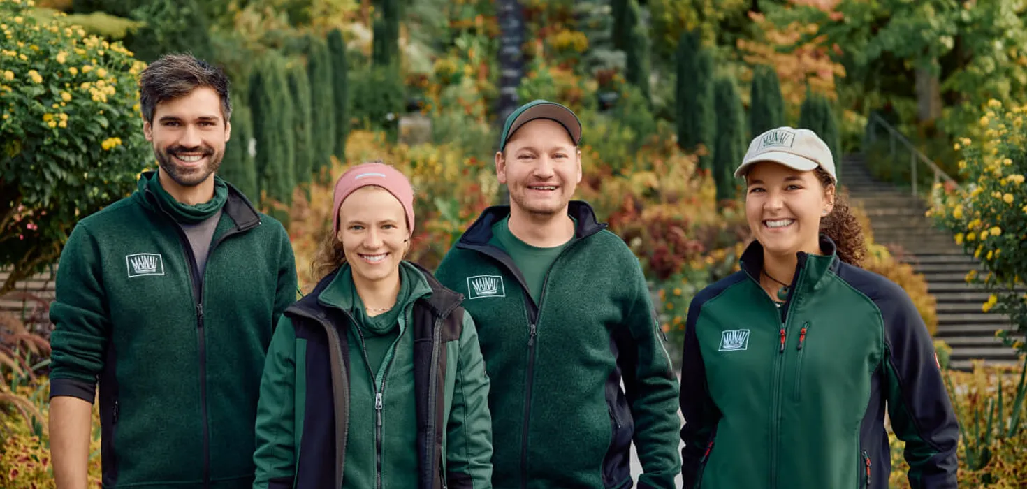 Team der Gärtnerinnen und Gärtner der Insel Mainau in Arbeitskleidung, umgeben von blühender Gartenpracht – stellvertretend für fachkundige Gartenpflege und grüne Kompetenz.
