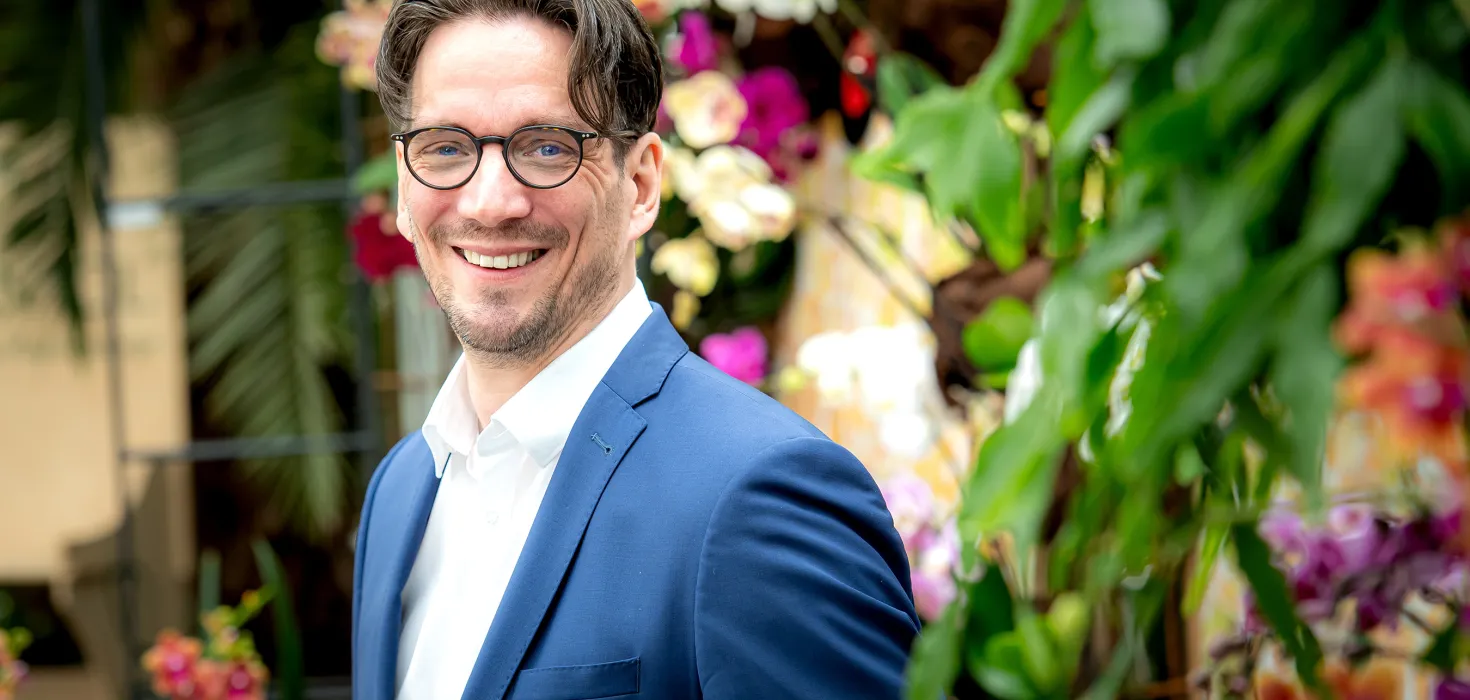 Ein Mann in einem blauen Anzug, der in einem Blumengarten lächelt.