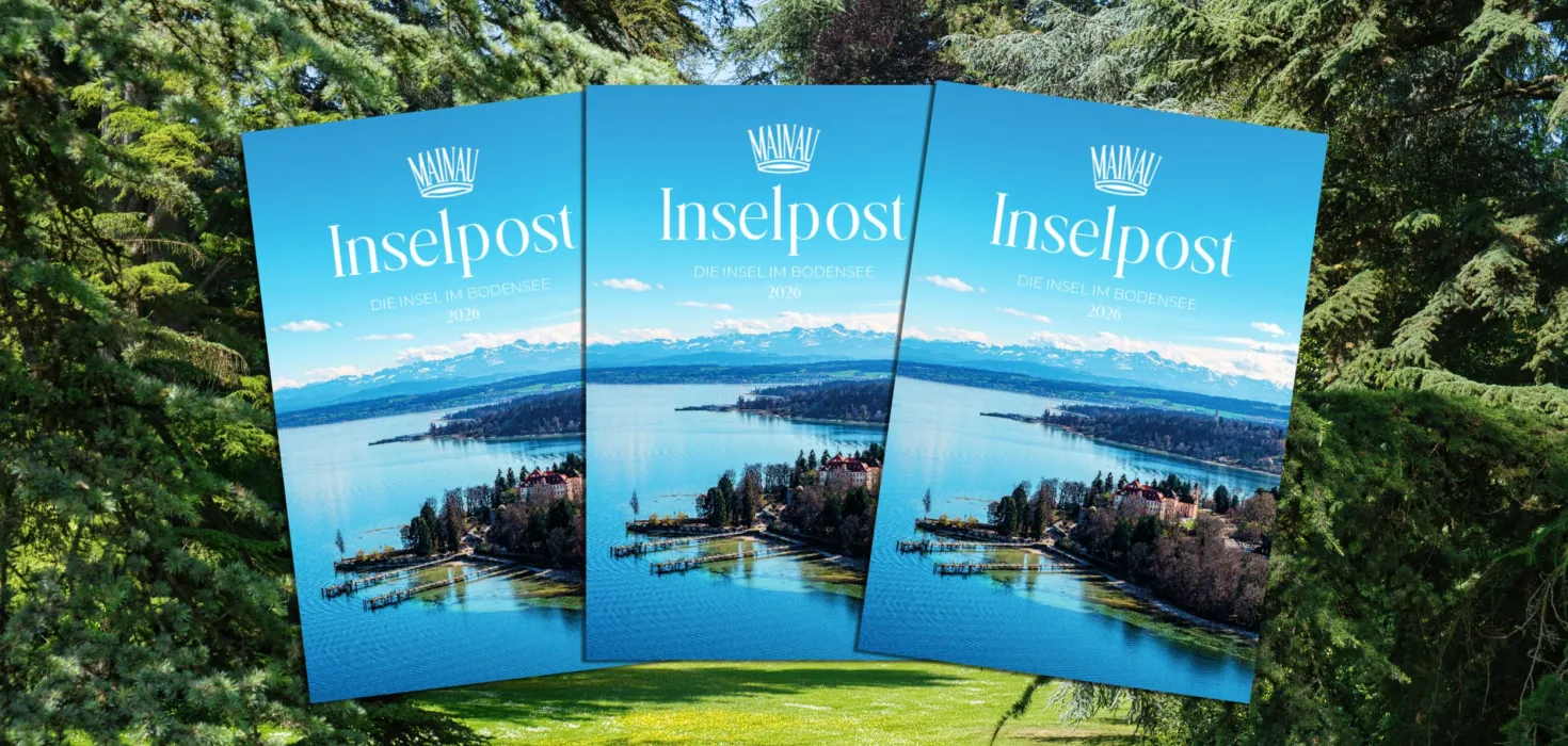 Drei Exemplare der Broschüre „Inselpost – Die Insel im Bodensee 2026“ der Insel Mainau, dargestellt vor einer Parklandschaft mit Bäumen und Wiese.