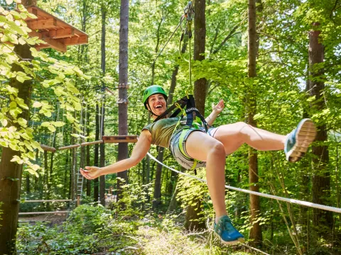 Junge Frau hängt fröhlich an einem Kletterseil und freut sich