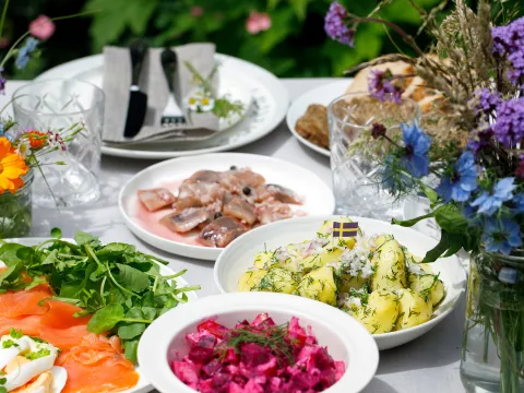 Tisch mit verschiedenen schwedischen Gerichten und einem Sommerblumenstrauß