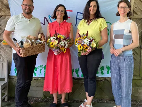 vier Personen, zwei davon mi Blumenstrauß und einer mit Geschenkkorb.