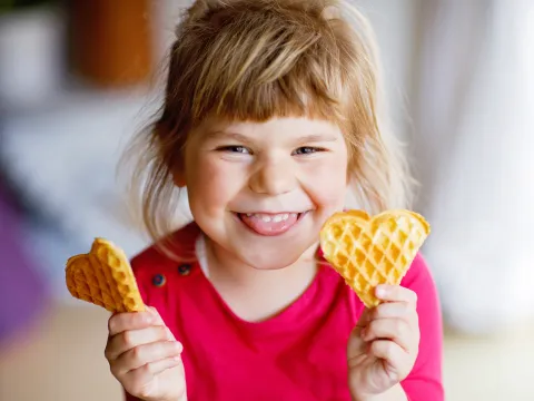 Mädchen mit zwei Waffeln in der Hand lacht in die Kamera