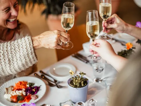 Drei Gläser Sekt werden in einem festlich gedeckten Tisch mit buntem Essen und Blumen in Töpfen angestoßen