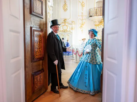 Zwei historisch gekleidete Personen öffnen die Türen zu einem herrschaftlichen Saal