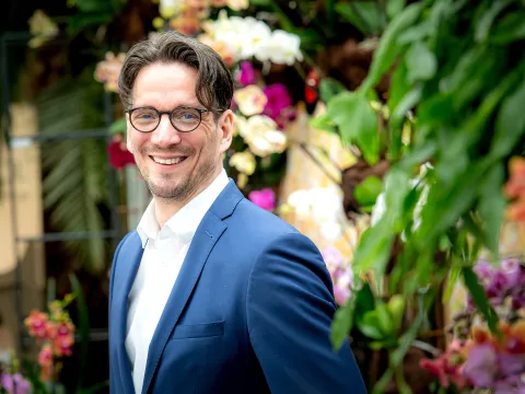 Ein Mann in einem blauen Anzug, der in einem Blumengarten lächelt.