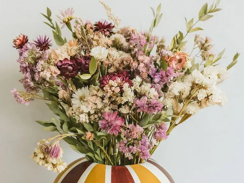 Bunter Blumenstrauß aus getrockneten Blüten in einer gestreiften Vase in warmen Gelb- und Brauntönen