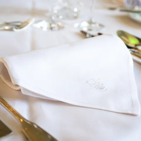 Festlich gedeckter Tisch mit weißer Stoffserviette und Mainau-Emblem