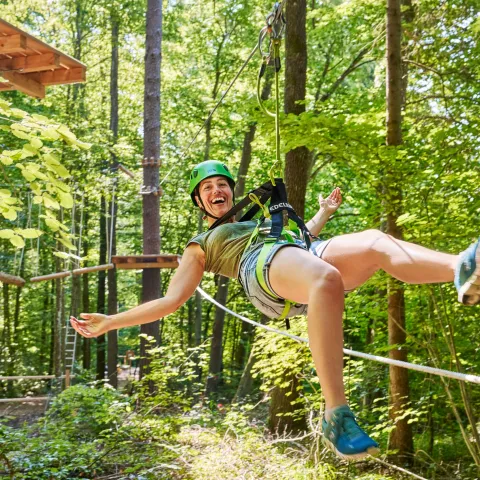 Junge Frau hängt fröhlich an einem Kletterseil und freut sich